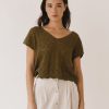 Mujer con top de punto calado en verde oliva, escote en V y manga corta, combinado con falda larga de lino beige