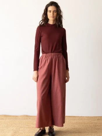 Mujer de pie con jersey de cuello alto y pantalón ancho en tonos granate