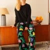 Mujer sentada descalza sobre un aparador, con jersey negro y pantalón floral multicolor